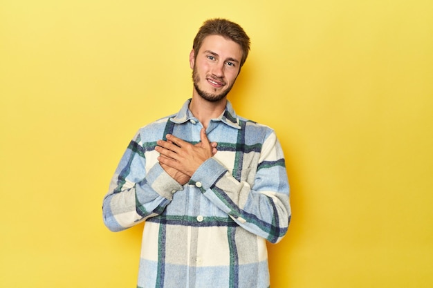 Young Caucasian man on a yellow studio background has friendly expression pressing palm to chest