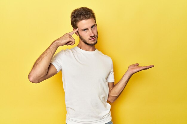 Foto giovane uomo caucasico su uno sfondo giallo studio che tiene e mostra un prodotto a portata di mano