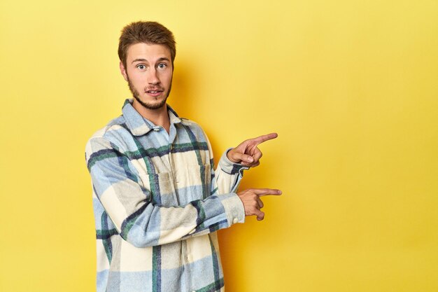 Photo young caucasian man on a yellow studio background shocked pointing with index fingers