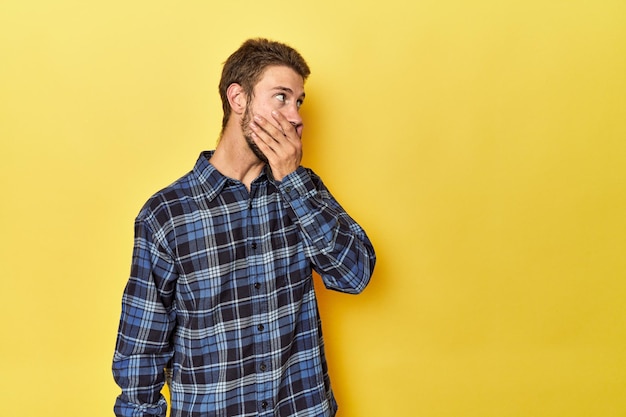 Young Caucasian man on a yellow studio background thoughtful looking to a copy space covering mouth