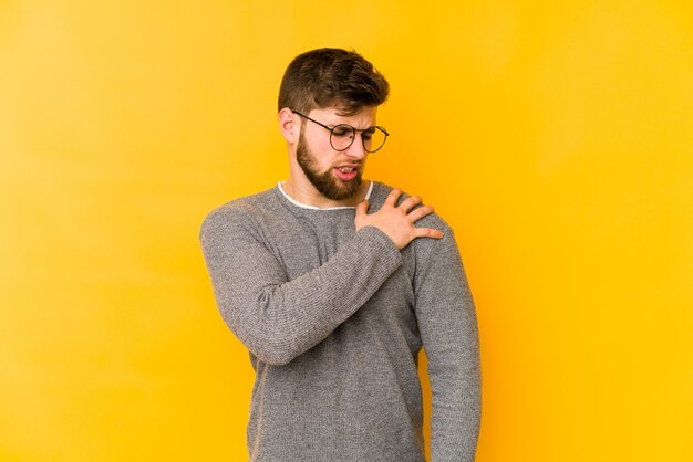 Young caucasian man on yellow wall having a shoulder pain.