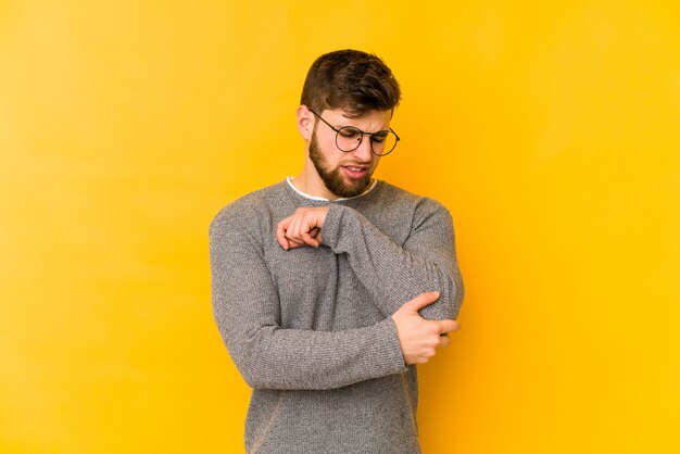 Young caucasian man on yellow wall massaging his elbow