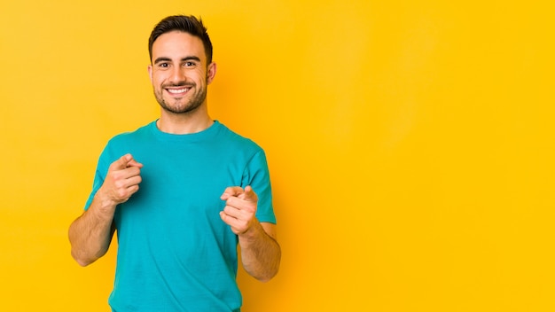 Young caucasian man on yellow wall pointing to front with fingers.