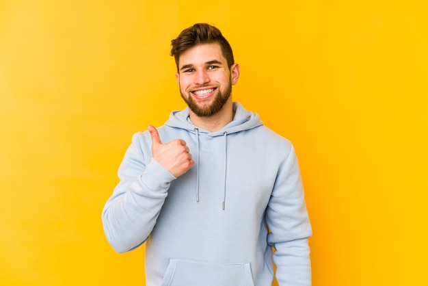 Young caucasian man on yellow wall smiling and raising thumb up
