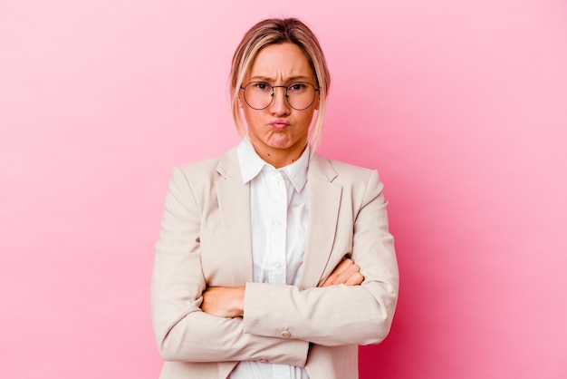 Young caucasian mixed race business woman isolated on pink wall blows cheeks, has tired expression. Facial expression concept.