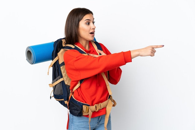 Young caucasian mountaineer girl with a big backpack on white pointing finger to the side