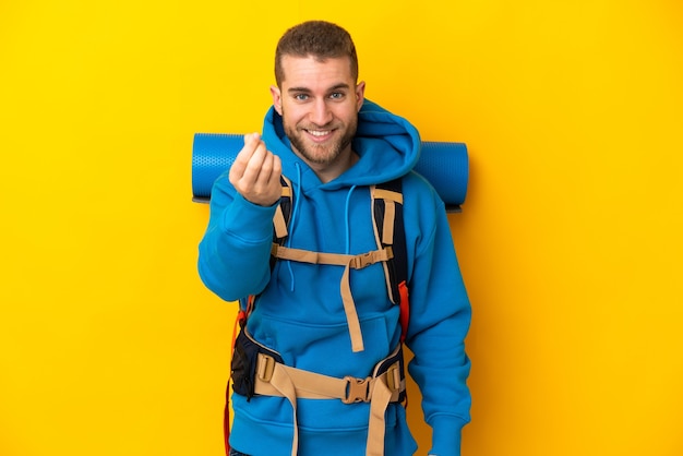 Uomo giovane alpinista caucasico con un grande zaino isolato sulla parete gialla che fa gesto di soldi