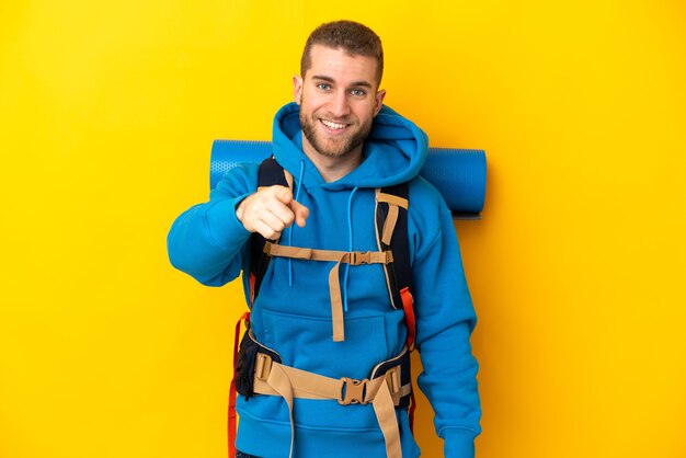 Young caucasian mountaineer man with a big backpack isolated on yellow wall surprised and pointing front