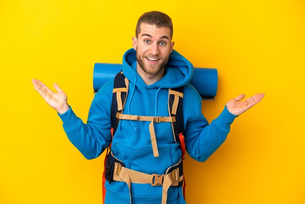 Young caucasian mountaineer man with a big backpack isolated on yellow wall with shocked facial expression