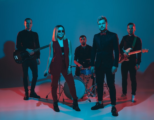 Young caucasian musicians, band performing in neon light on blue studio background