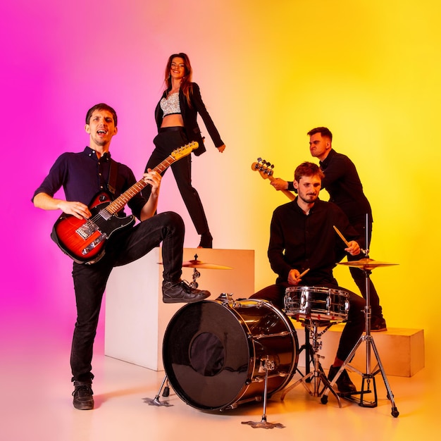 Young caucasian musicians, band performing in neon light on gradient studio background