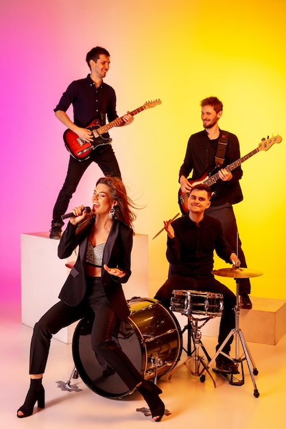 Young caucasian musicians, band performing in neon light on gradient studio background