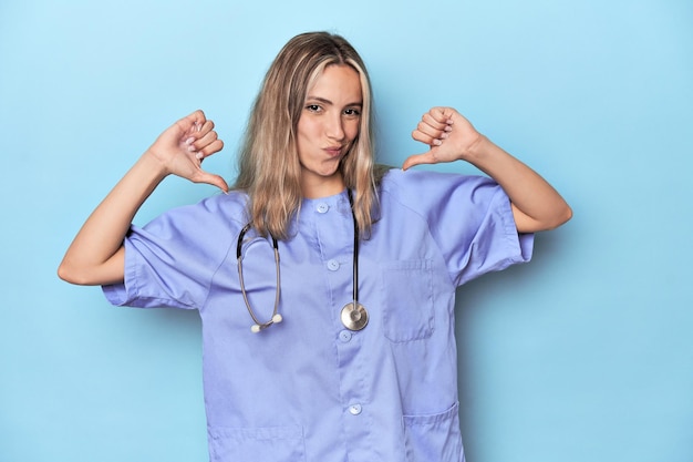 Young caucasian nurse in blue studio feels proud and self confident example to follow