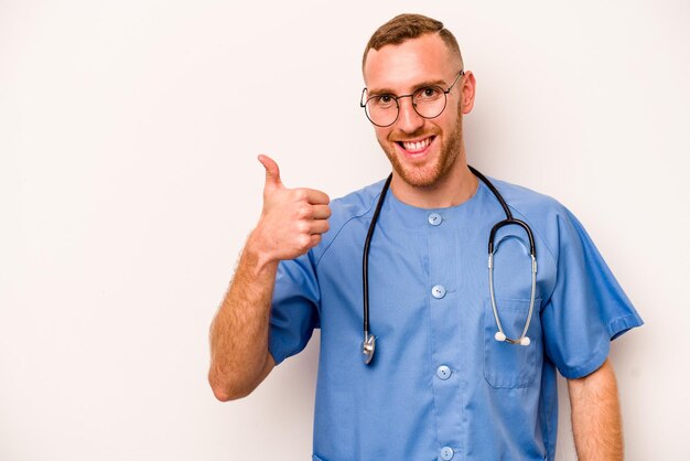 웃 고 엄지손가락을 올리는 흰색 배경에 고립 된 젊은 백인 간호사 남자