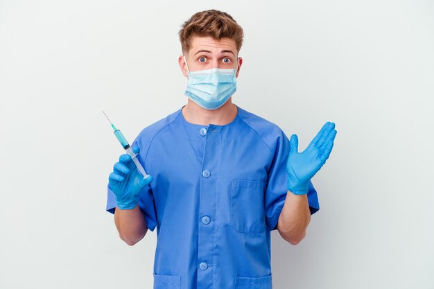 Young caucasian nurse man prepared to give a vaccine isolated on white background surprised and shocked.