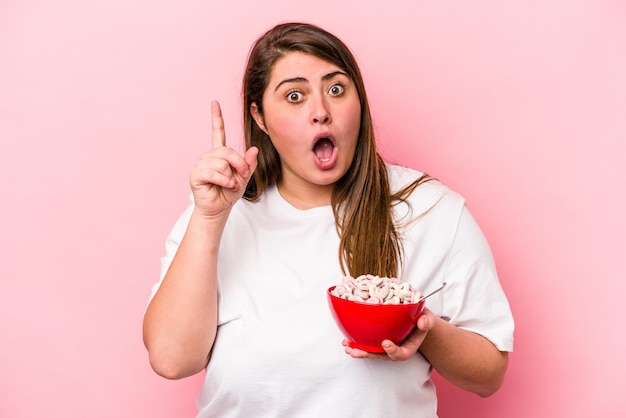 Foto giovane donna caucasica sovrappeso che tiene una ciotola di cereali isolata su sfondo rosa con un'idea, concetto di ispirazione.