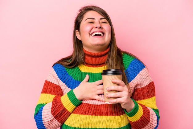 Young caucasian overweight woman holding takeaway coffee isolated on pink background laughs out loudly keeping hand on chest.