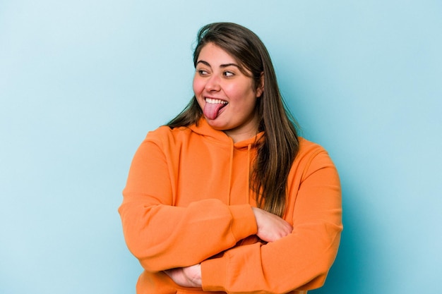 Young caucasian overweight woman isolated on blue background funny and friendly sticking out tongue