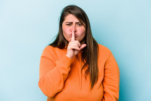 Young caucasian overweight woman isolated on blue background keeping a secret or asking for silence