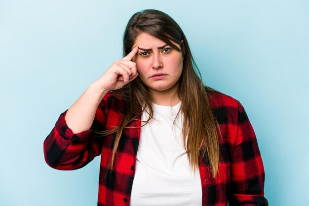 Young caucasian overweight woman isolated on blue background pointing temple with finger thinking focused on a task
