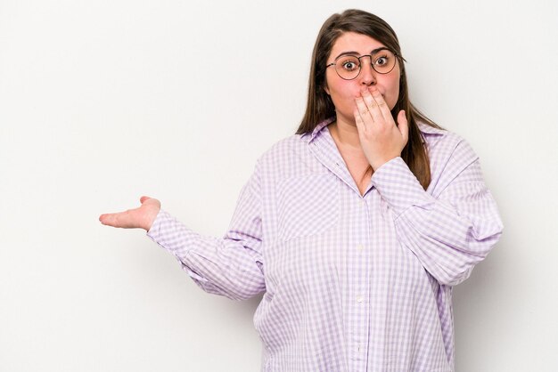 Young caucasian overweight woman isolated on white background impressed holding copy space on palm