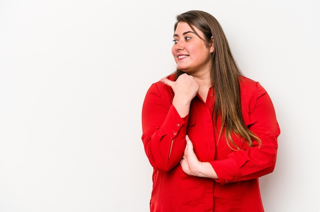 Young caucasian overweight woman isolated on white background points with thumb finger away, laughing and carefree.