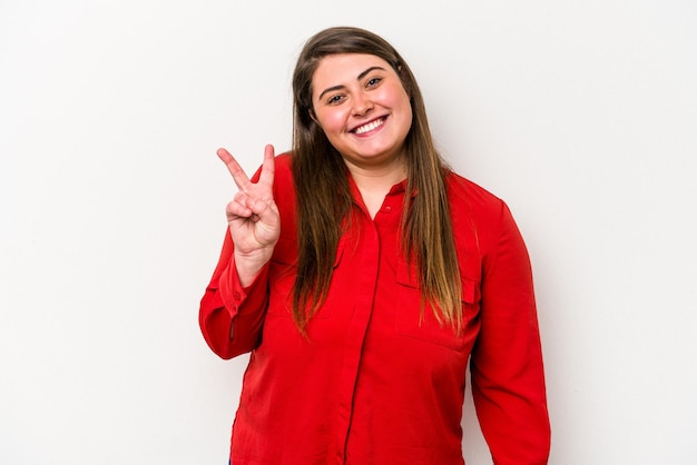 Young caucasian overweight woman isolated on white background showing victory sign and smiling broadly.