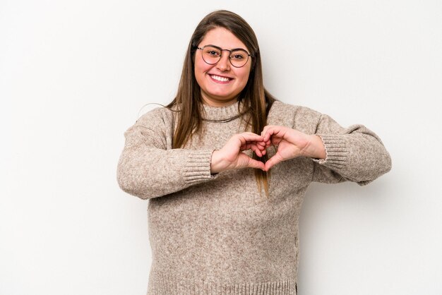 Young caucasian overweight woman isolated on white background smiling and showing a heart shape with hands