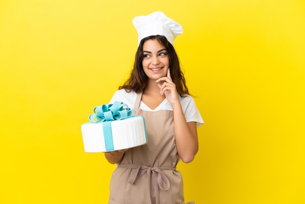 Young caucasian pastry chef woman with a big cake isolated on yellow background thinking an idea while looking up