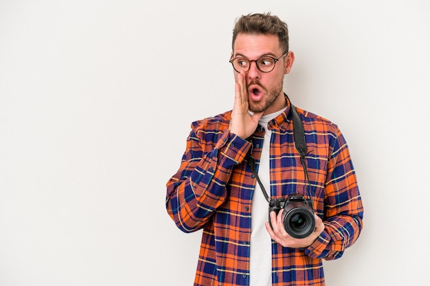 Young caucasian photograph man isolated on white background is saying a secret hot braking news and looking aside