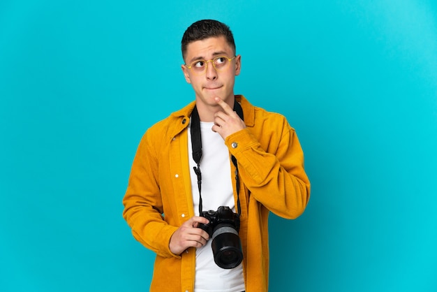 Молодой кавказский фотограф человек на синем, сомневаясь и думая