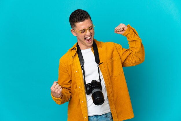 Young  caucasian photographer man isolated on blue celebrating a victory