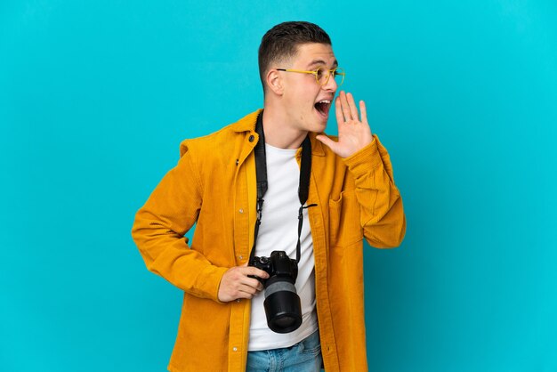 Young  caucasian photographer man isolated on blue shouting with mouth wide open to the side