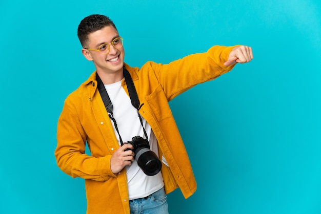 親指を立てるジェスチャーを与える青い壁に分離された若い白人写真家の男