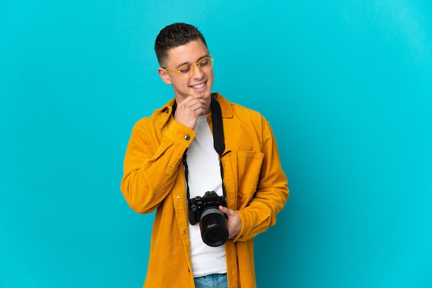 Young  caucasian photographer man isolated on blue wall looking to the side and smiling