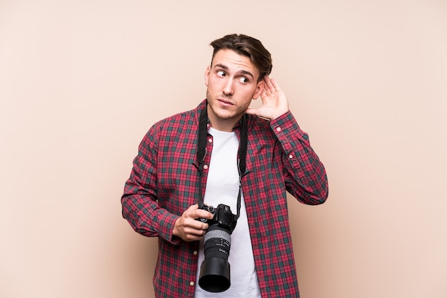 Young caucasian photographer man isolated trying to listening a gossip.