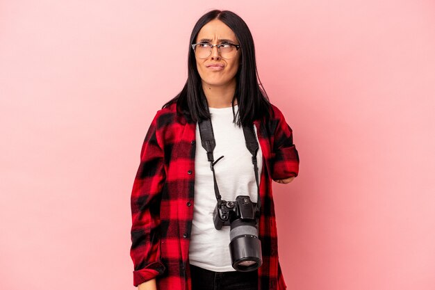 Young caucasian photography woman with one arm isolated on pink background confused, feels doubtful and unsure.