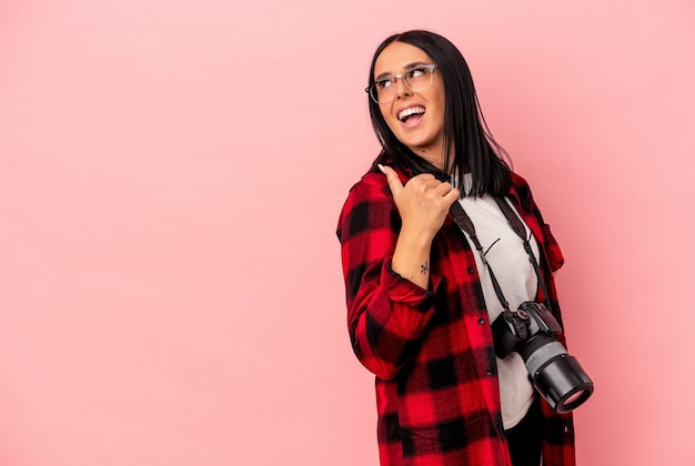 Young caucasian photography woman with one arm isolated on pink background points with thumb finger away, laughing and carefree.