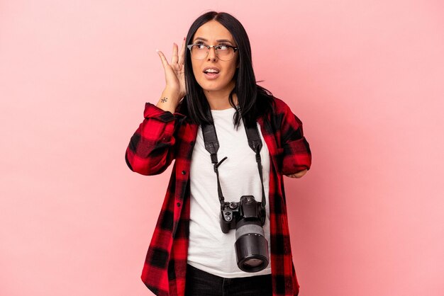 Young caucasian photography woman with one arm isolated on pink background trying to listening a gossip.