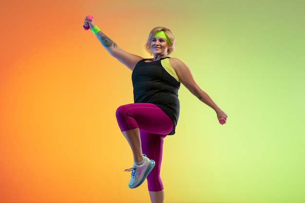 Young caucasian plus size female model's training on gradient orange wall in neon light. 