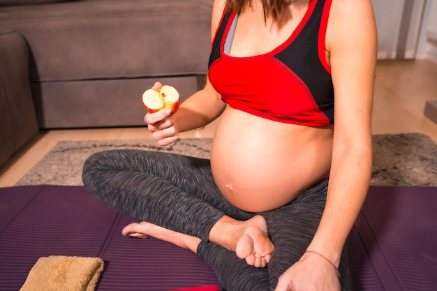 Young caucasian pregnant female eating an apple after an online yoga class
