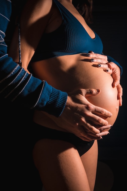 Giovane donna incinta caucasica che sta per partorire. con le mani di suo padre e di sua madre sulla pancia del bambino. in alcune foto in studio