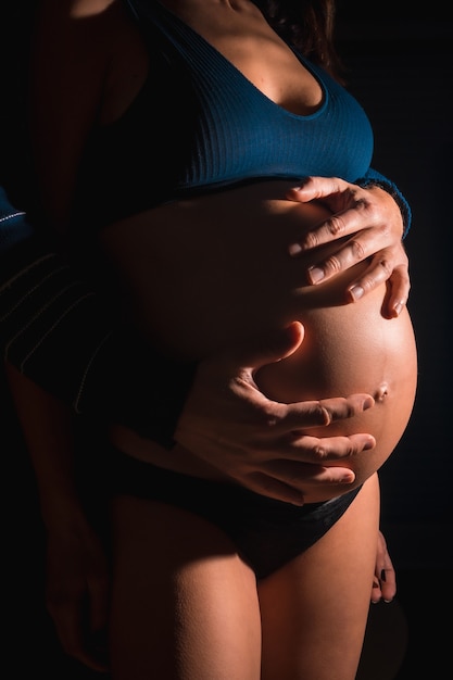 Young Caucasian pregnant woman about to give birth. With the hands of her father and her mother on the baby's belly. In some studio photos