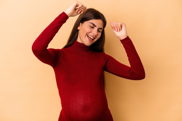 Young caucasian pregnant woman isolated on beige wall celebrating a special day, jumps and raise arms with energy.