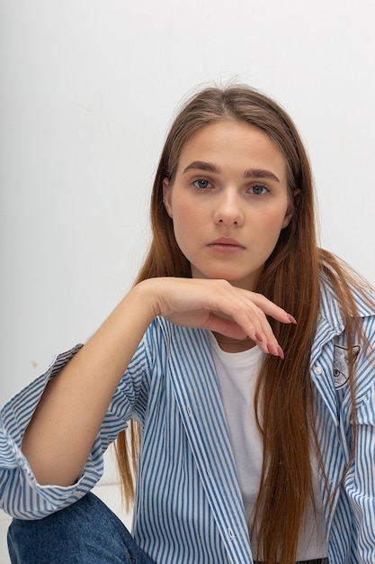 Young caucasian pretty girl with long hair in blue striped shirt sits at studio