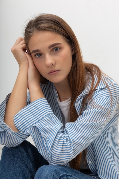 Young caucasian pretty girl with long hair in blue striped shirt sits at studio