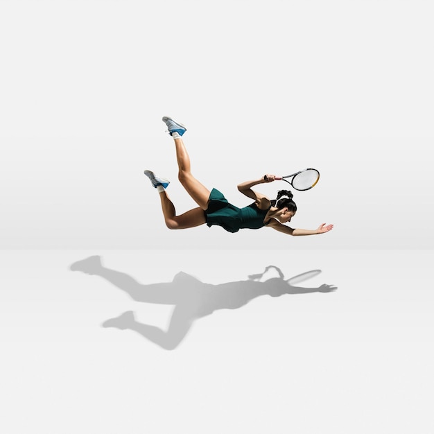 白い背景で隔離のテニスをしながら飛んで浮揚する若い白人プロスポーツウーマン