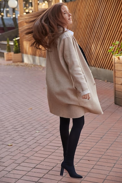 Young caucasian red headed girl in coat with long hair spinning around at place