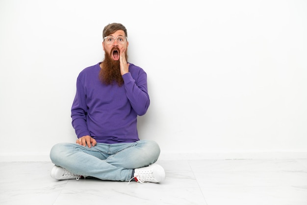 Young caucasian reddish man sitting on the floor isolated on white background with surprise and shocked facial expression