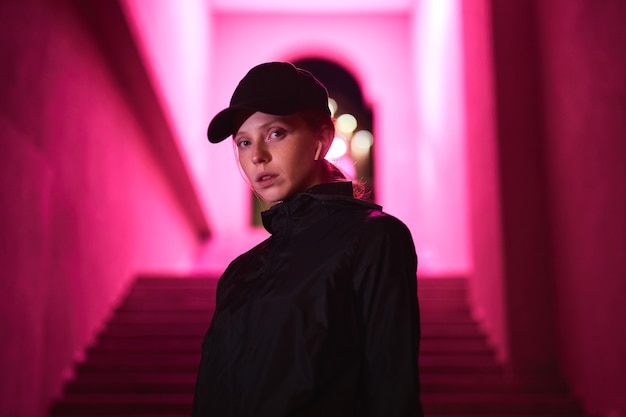 Young caucasian redhead female in black cap sportive clothes and headphones walking outdoors in nigh...